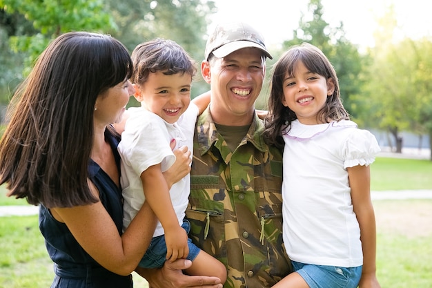 Happy military man posing with his family, holding kids in arms, his wife hugging all of them and laughing. Medium shot. Family reunion or returning home concept