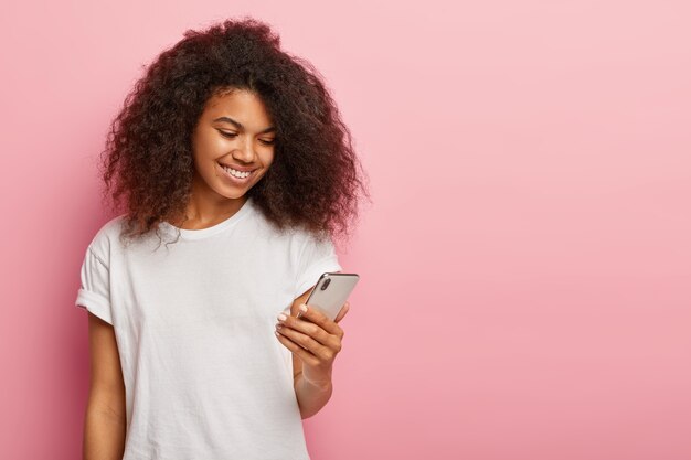 Happy millennial Afro American woman with dark curls, watches funny video on smart phone