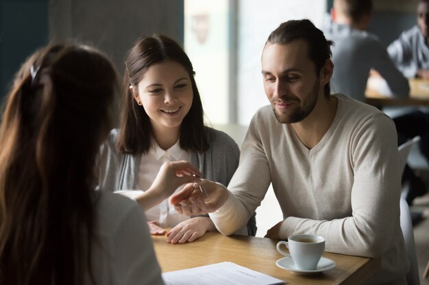 Happy millennial couple getting keys to new house from realtor