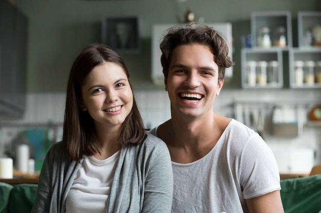 Happy millennial couple looking at camera in kitchen, headshot portrait
