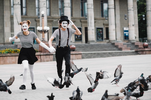 Happy mime couple running near flying pigeons