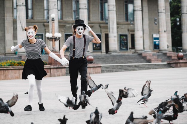 Happy mime couple running near flying pigeons