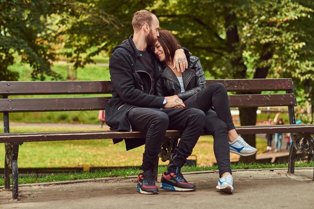 Happy modern couple cuddling on a bench in the park. Enjoying their love and nature.