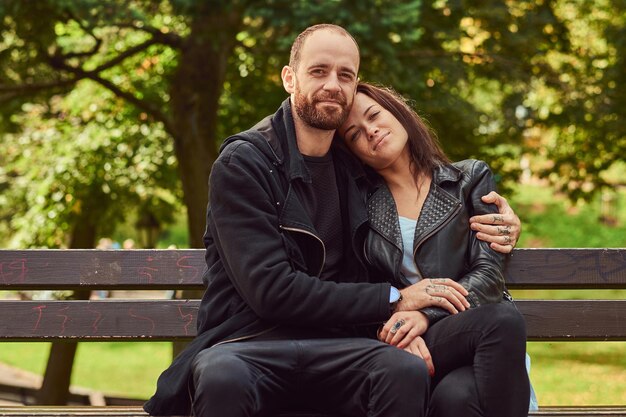 Happy modern couple cuddling on a bench in the park. Enjoying their love and nature.