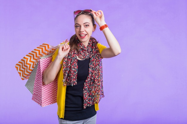 Free photo happy modern woman holding decorative paper bag in front of purple wall