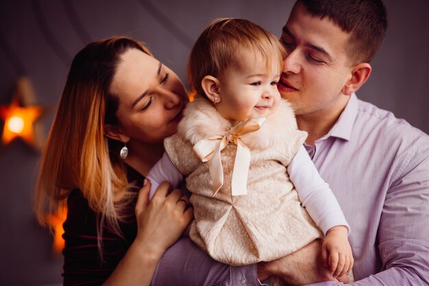 Happy mom and dad hold charming little girl in their arms