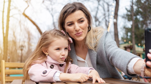 Mamma felice e figlia che prendono selfie all'aperto