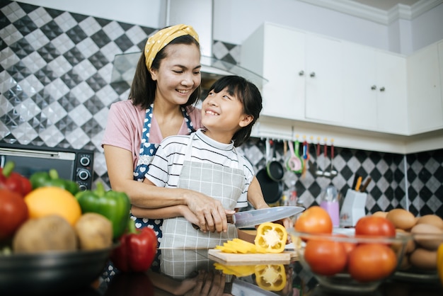 Happy mom teaching her daughter preparing and chopping vegetable for cooking. 