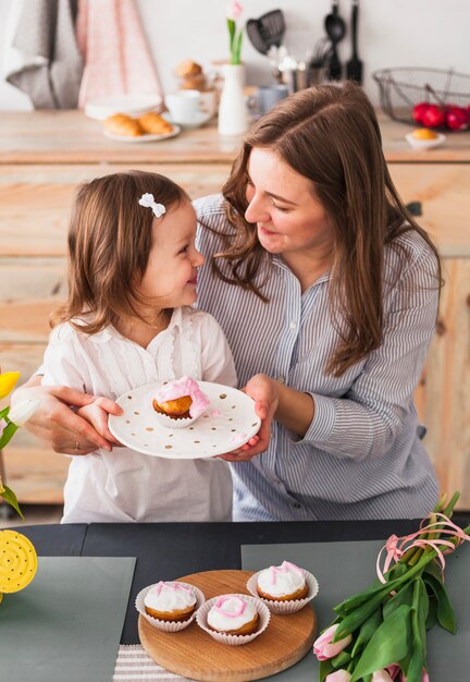 幸せな母と娘のカップケーキとプレートを保持