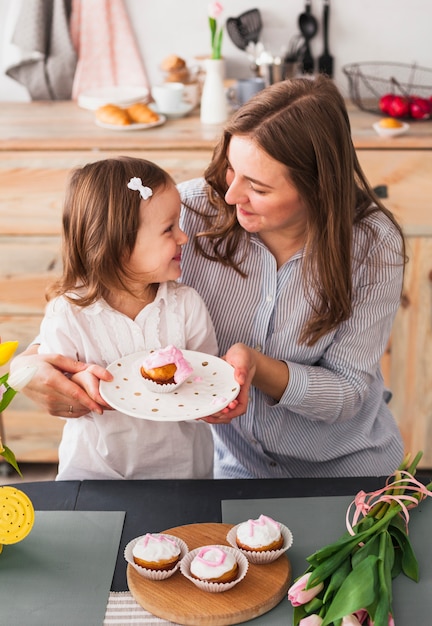 Happy mother and daughter holding plate with cupcake