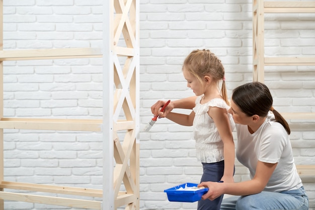 Happy mother and daughter painting wooden shelves