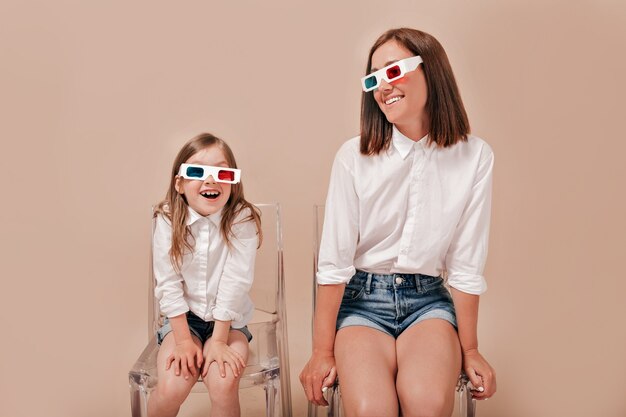Happy mother and daughter sitting over beige background, having fun and laughing.