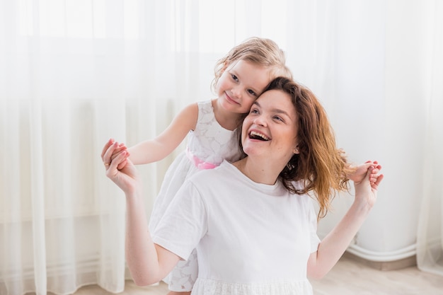 Happy mother and daughter sitting in front of white curtain
