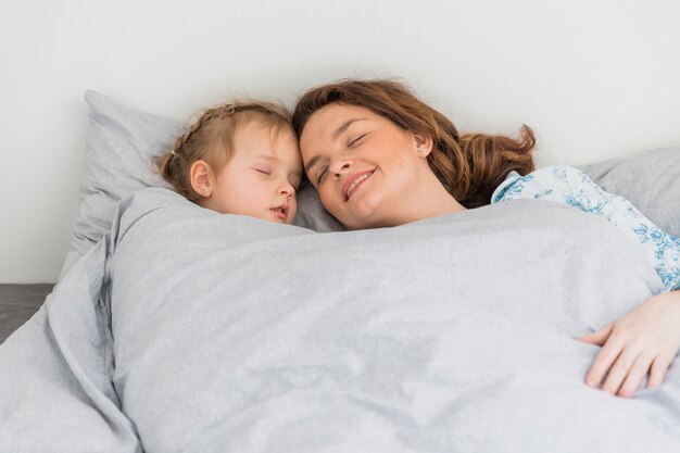 Happy mother and daughter sleeping together in home