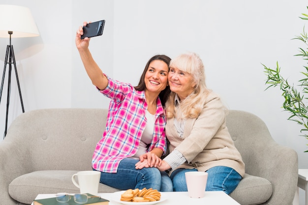 幸せな母と娘のテーブルの上の朝食付き携帯電話にselfieを取って