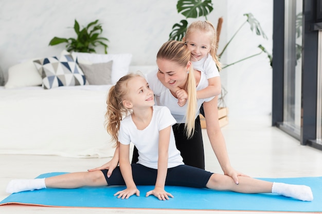 Happy mother and daughters at home on yoga mat