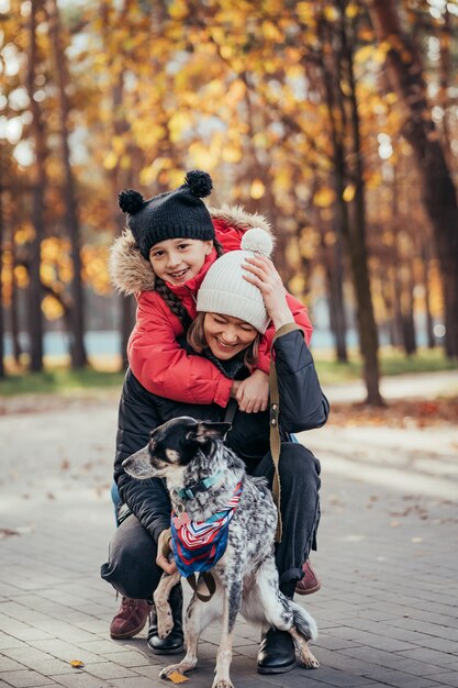 幸せな母と娘が秋の公園で犬と遊んで