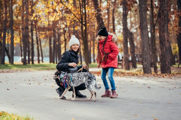 Happy mother and her daughter playing with dog in autumn park