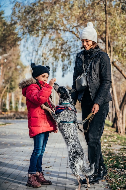 Happy mother and her daughter playing with dog in autumn park