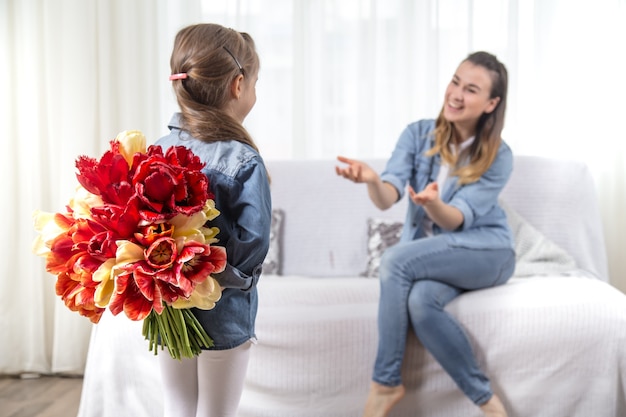 С днем матери. маленькая милая дочка с большим букетом тюльпанов поздравляет маму. в интерьере гостиной концепция счастливой семейной жизни