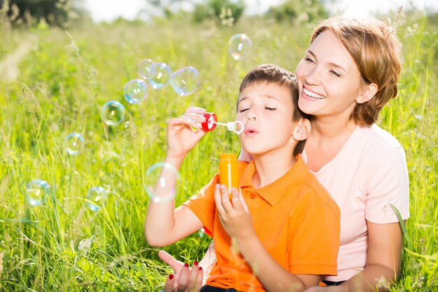 Счастливая мать и сын в парке, дует мыльные пузыри на открытом воздухе портрет