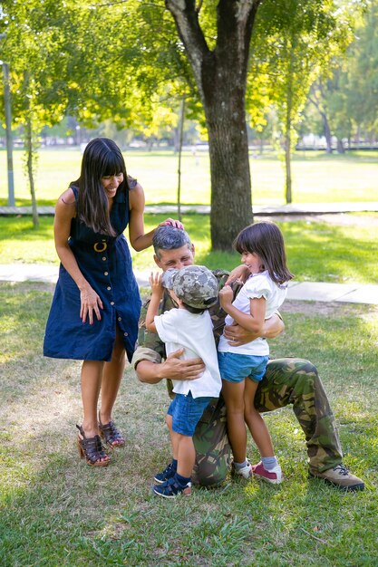 행복 한 어머니와 위장 유니폼 야외에서 군사 아버지를 포옹하는 두 아이. 세로 샷. 가족 상봉 또는 귀국 개념