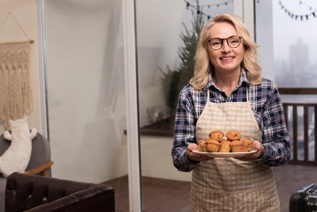 Happy mother with apron holding plate of muffins