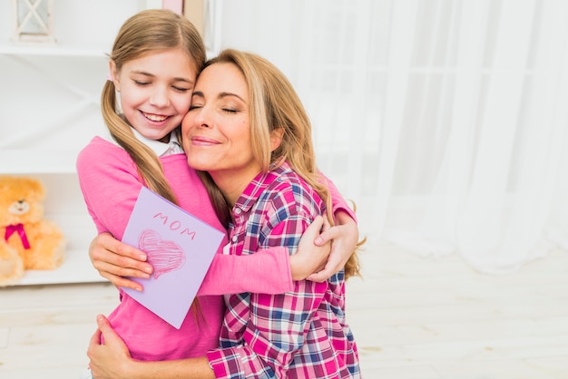 Happy mother with greeting card hugging daughter 