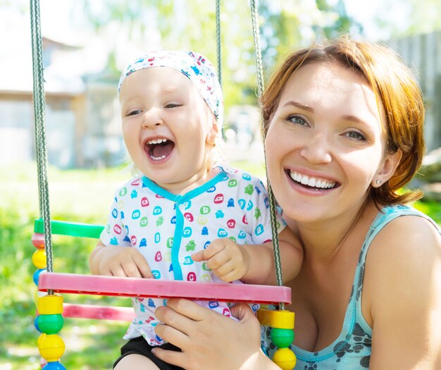 Happy mother with laughing baby sits on the swing