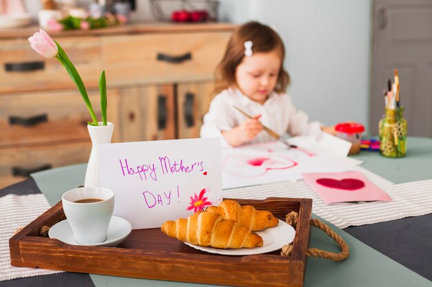 Happy Mothers Day inscription on table near girl painting heart