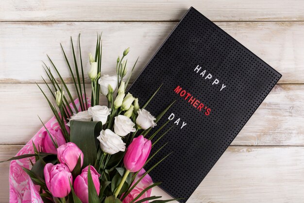 Happy mothers day title on board near bouquet of flowers