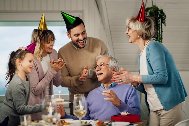 Счастливая семья из нескольких поколений поет во время празднования дня рождения пожилого человека в столовой