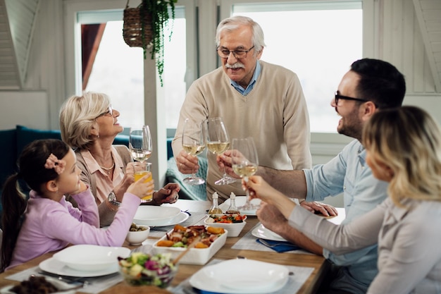Happy multigeneration family toasting while having lunch together at dining table Focus is on senior man
