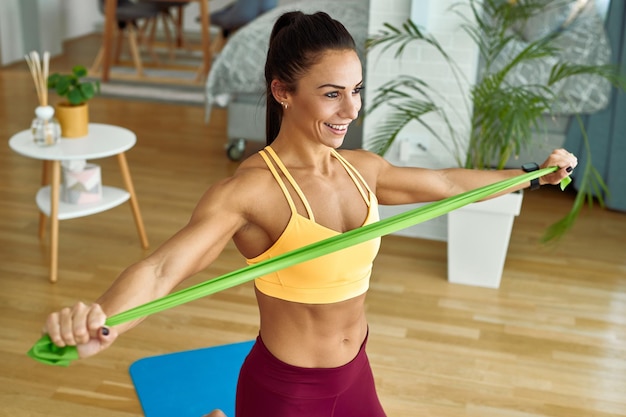 Счастливая мускулистая женщина тренируется дома с лентой сопротивления