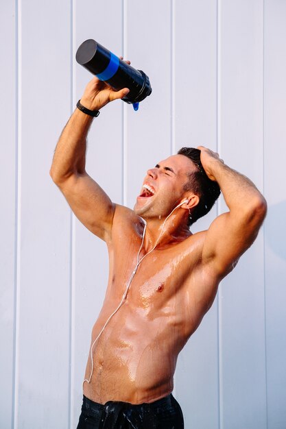 счастливый мускулистый парень, выливающий воду из бутылки на свое тело, потение после тренировки