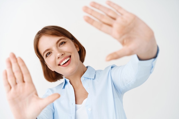 Happy natural girl with short hair, dreaming, stretch out hands, capture and enjoy moment, standing on white wall