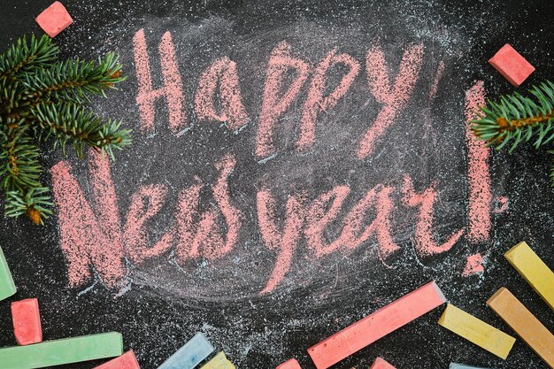 Happy New Year - background or a postcard. Happy new year lettering chalk on a school board. Gift mock-up board decorated with fir branches. View from above