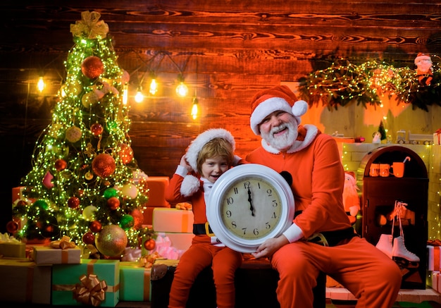 작은 조수가 있는 새해 복 많이 받으세요 산타는 산타클로스로 옷을 입은 오래된 시계 아이를 기다리고 있습니다