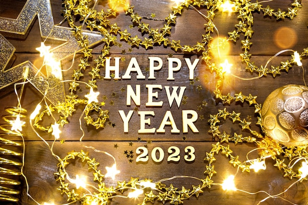 Premium Photo | Happy New Year-Wooden Letters And The Numbers 2023 On A Festive Background With Sequins, Stars, Glitter, Lights Of Garlands. Greetings, Postcard. Calendar, Cover