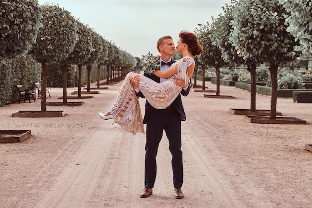 Foto gratuita felici sposi novelli. lo sposo bello tiene la sua sposa affascinante tra le braccia nel fantastico giardino.