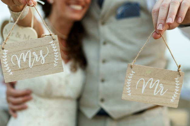 Happy newlyweds hold wooden boards with letterings 'Mrs' and 'Mr'