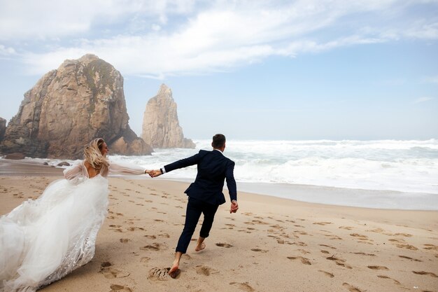 大西洋のビーチを横切って手を取り合って幸せな新婚夫婦