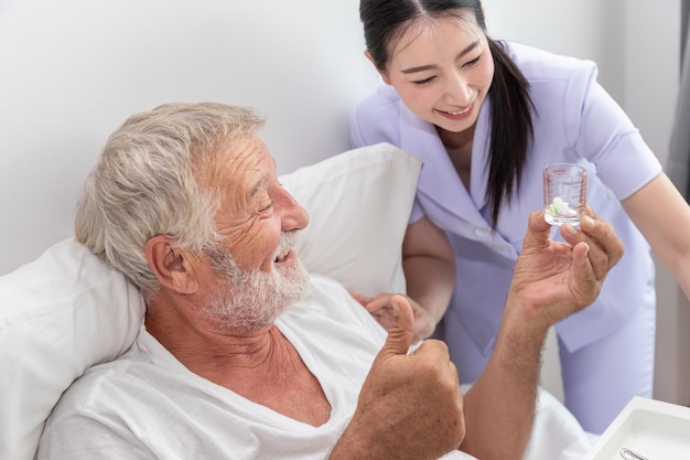 L'infermiera felice dà le pillole per aiutare e incoraggiare l'anziano anziano a mangiare medicine dopo la colazione sul letto nella camera da letto della casa di cura