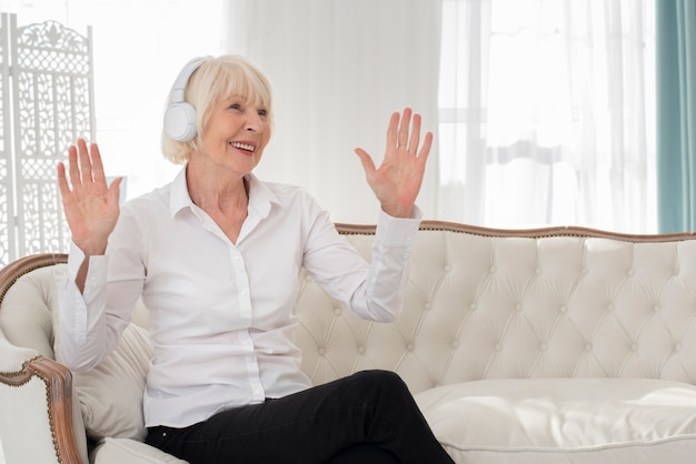 Happy old woman sitting on sofa with headphones