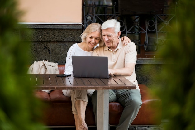 Happy older couple sitting on bench outdoors with laptop