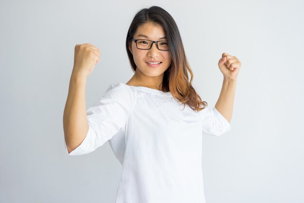 Happy optimistic young Asian woman in eyeglasses showing her power 