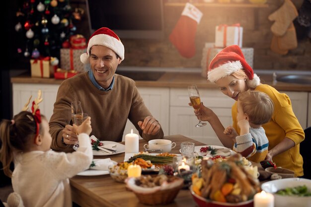 ダイニングテーブルで小さな子供たちとクリスマスランチを楽しんで幸せな親