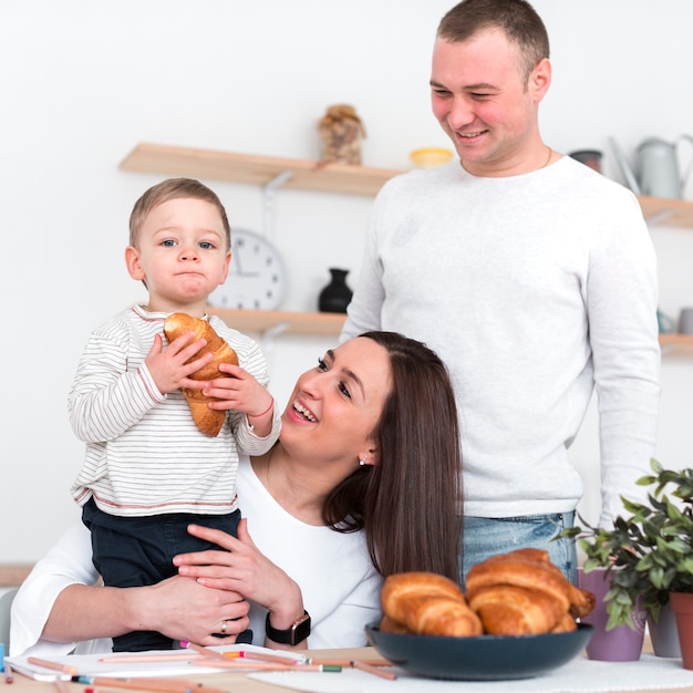 Бесплатное фото Счастливые родители держа ребенка с круассаном