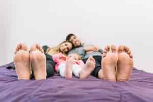 Free photo happy parents lying with their daughter on bed