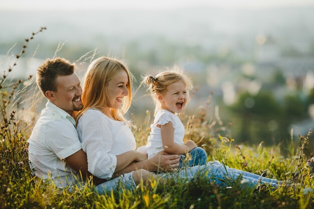 Happy parents and their little girl rest on the lawn in beautiful summer day